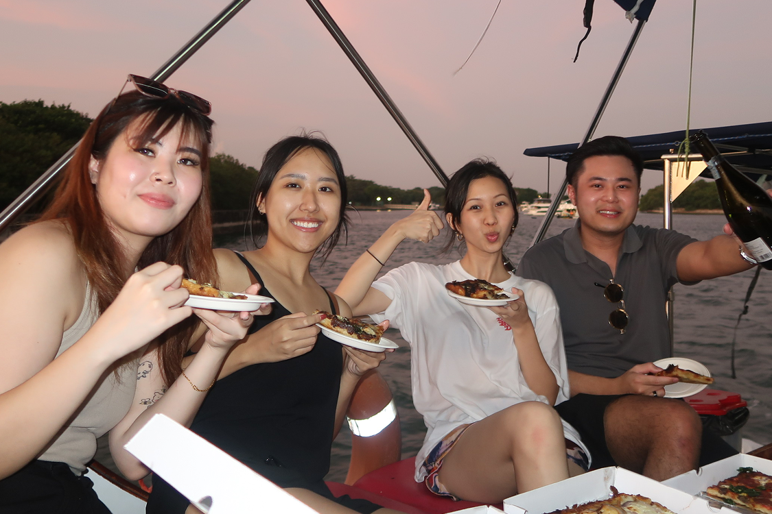 Four colleagues sharing pizza on a boat at sunset