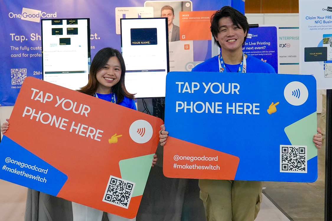 Two team members holding oversized Tap Your Phone Here boards at an event