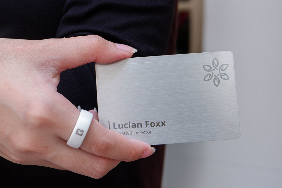 Brushed steel metal NFC business card displayed alongside a One Good Ring smart NFC ring